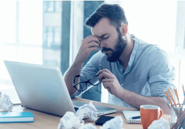 A man sitting at a table with his head down looking at the laptop.