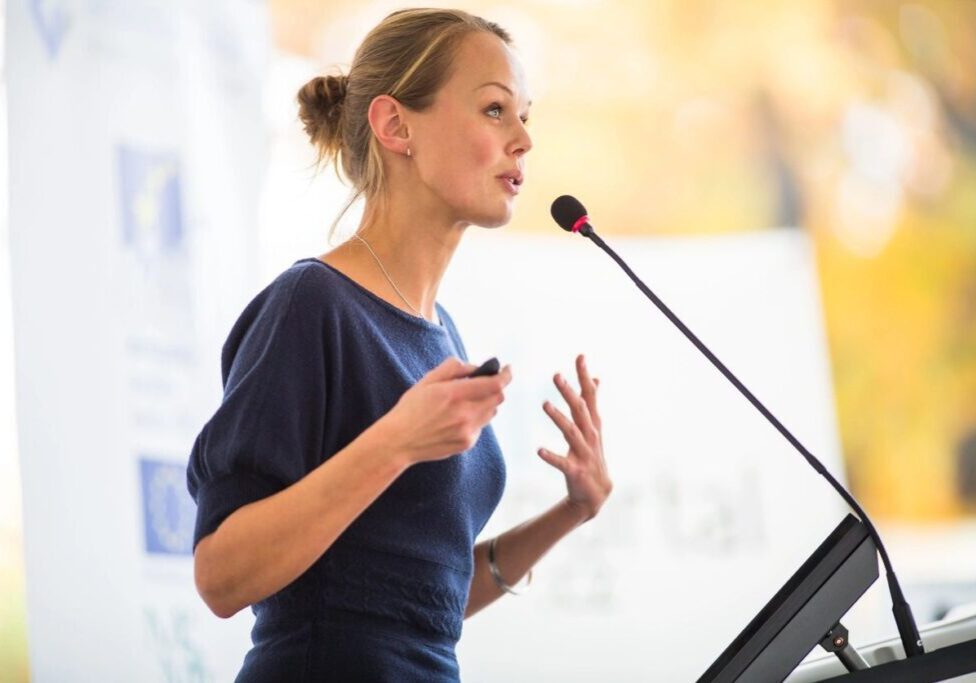 A woman is speaking at a podium with her hands raised.